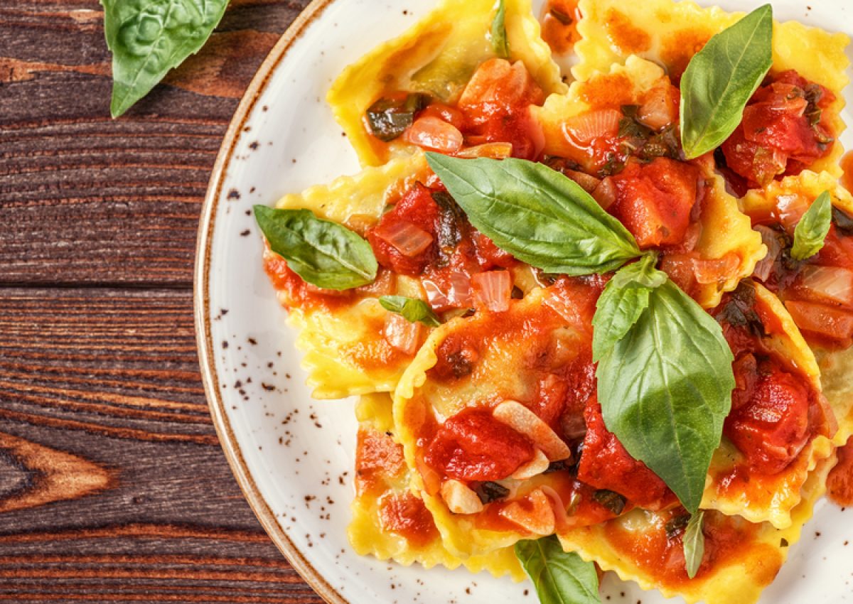 Ravioli with tomato sauce and basil on dark background, top view.