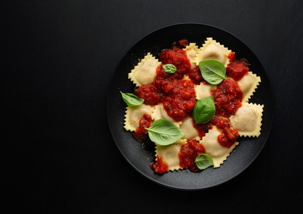 Tasty cooked italian ravioli with tomato sauce and basil served on dark plate.